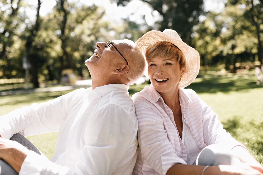 trendy-short-haired-lady-in-light-hat-and-striped-blouse-smiling-and-sitting-on-grass-with-old-man-in-glasses-and-white-shirt-outdoor--Bioidentical-Hormone-Replacement-Therapy